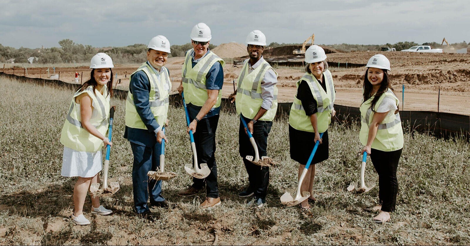 A group of people in hard hats and safety vests breaking ground with shovels