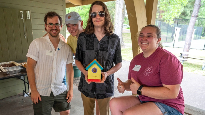 Four AmeriCorps members posing with a birdhouse at a staff picnic.