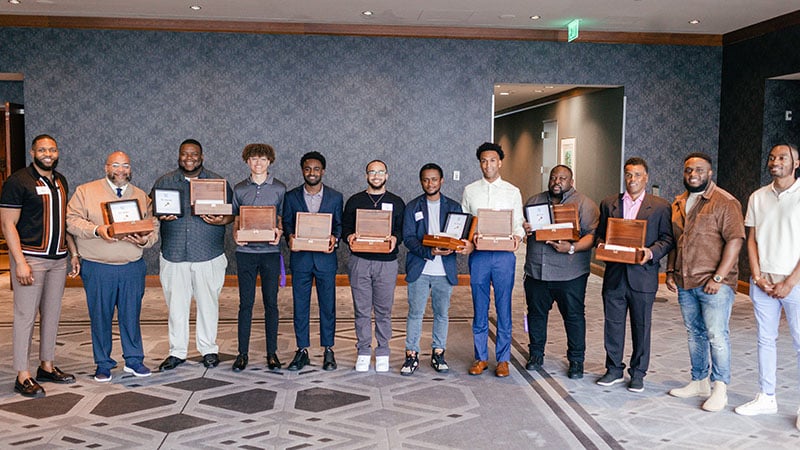 Participants with Black Men Teach standing in a row with plaques 