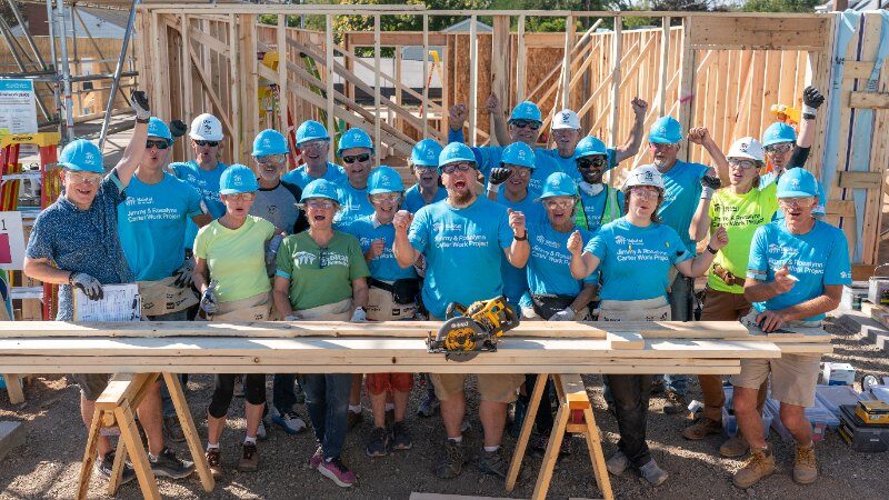 Group of volunteers posing in front of their house frame.