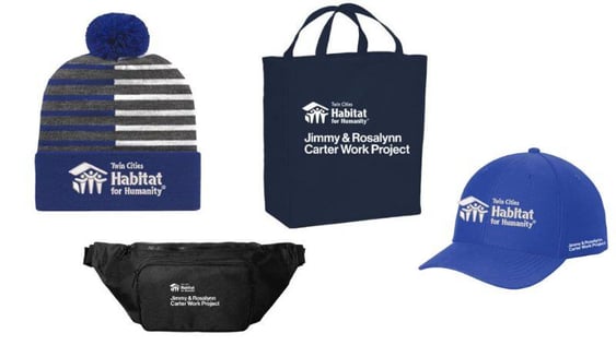 A blue baseball cap and blue striped beanie hat with the TC Habitat logo, and both a blue tote bag and black fanny pack with the Carter Work Project and Habitat logos.