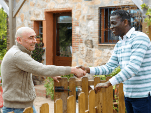 Neighbors shaking hands over a fence.