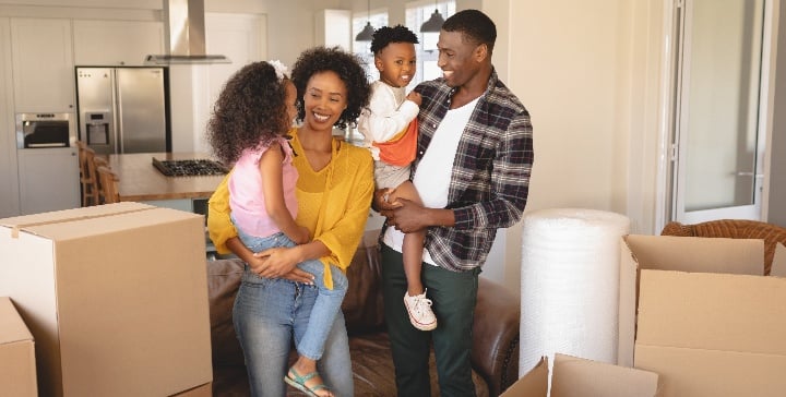 Two parents holding their kids in their home and smiling.