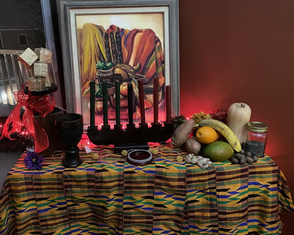 A festive Kwanzaa altar with 7 candles, a variety of produce and nuts, and gifts.