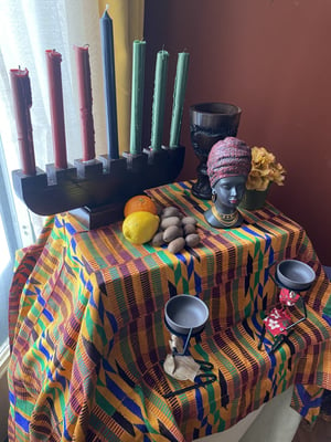 A Kwanzaa altar with candles, goblets, decorative figures, and produce.