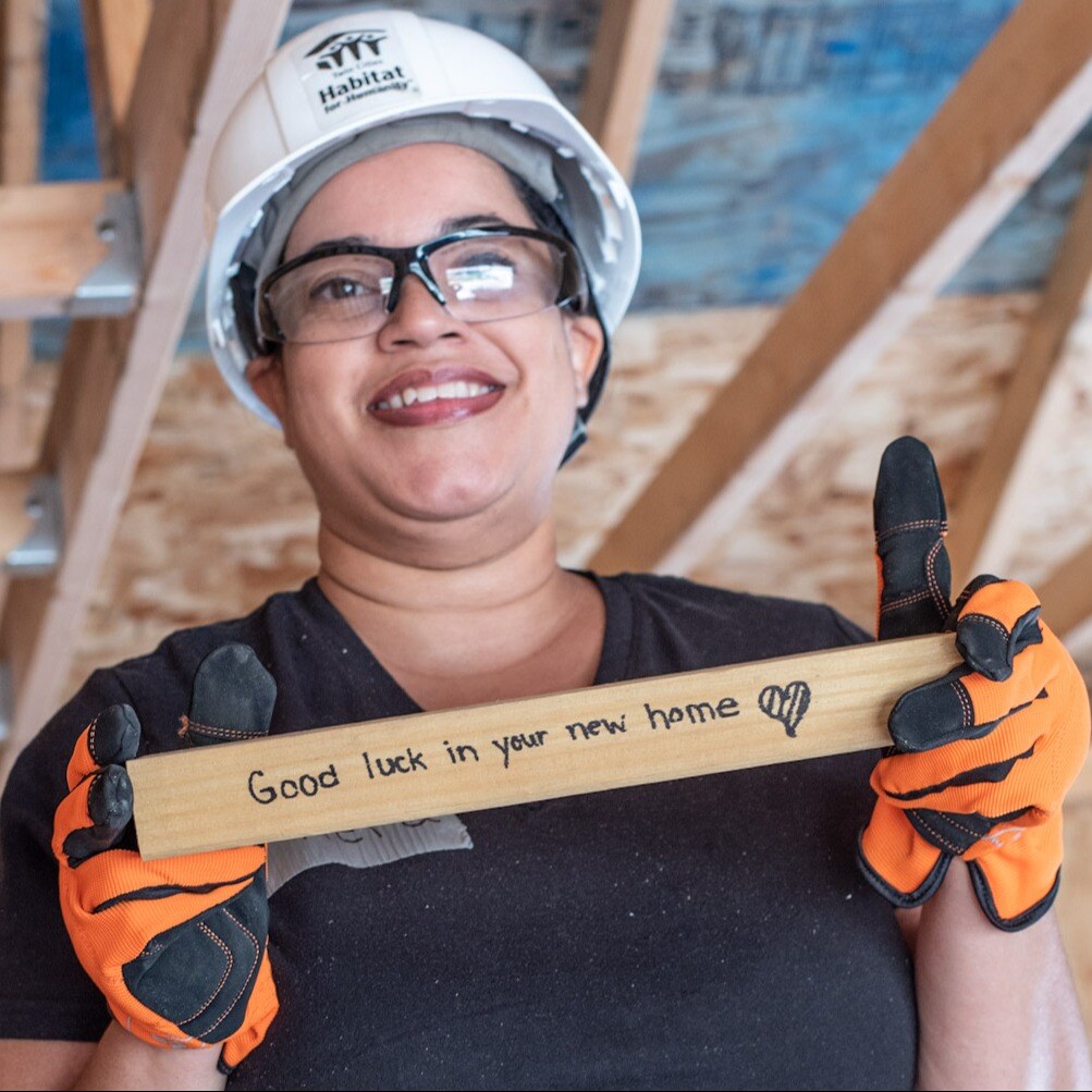 A woman holding a plank of wood that says good luck in your new home